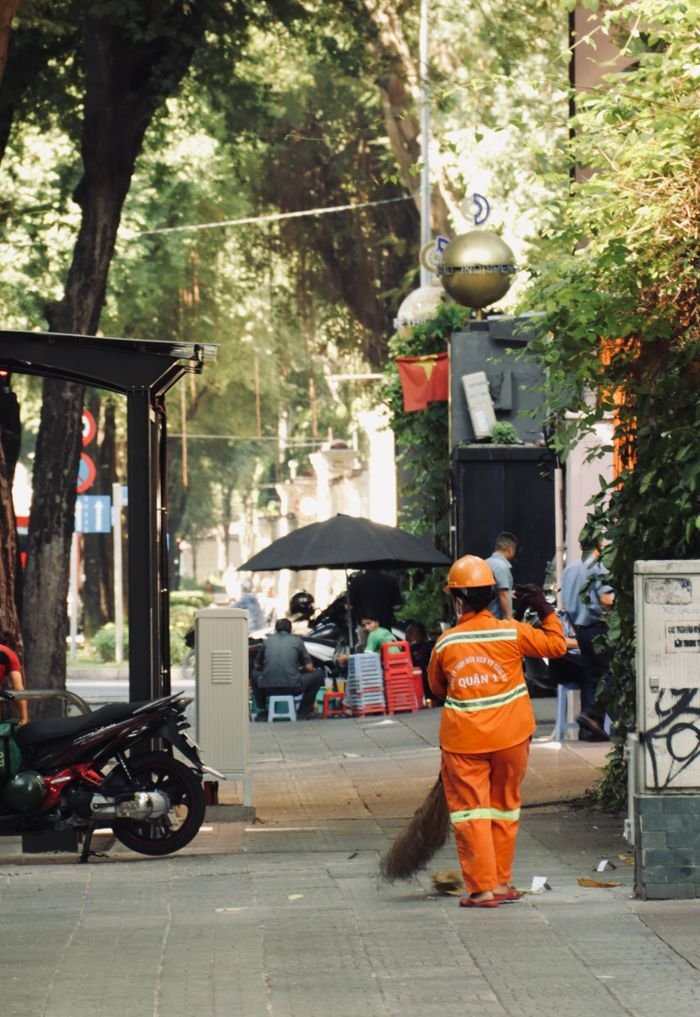 Street worker cleaning a colorful city street surrounded by lush greenery and urban elements.